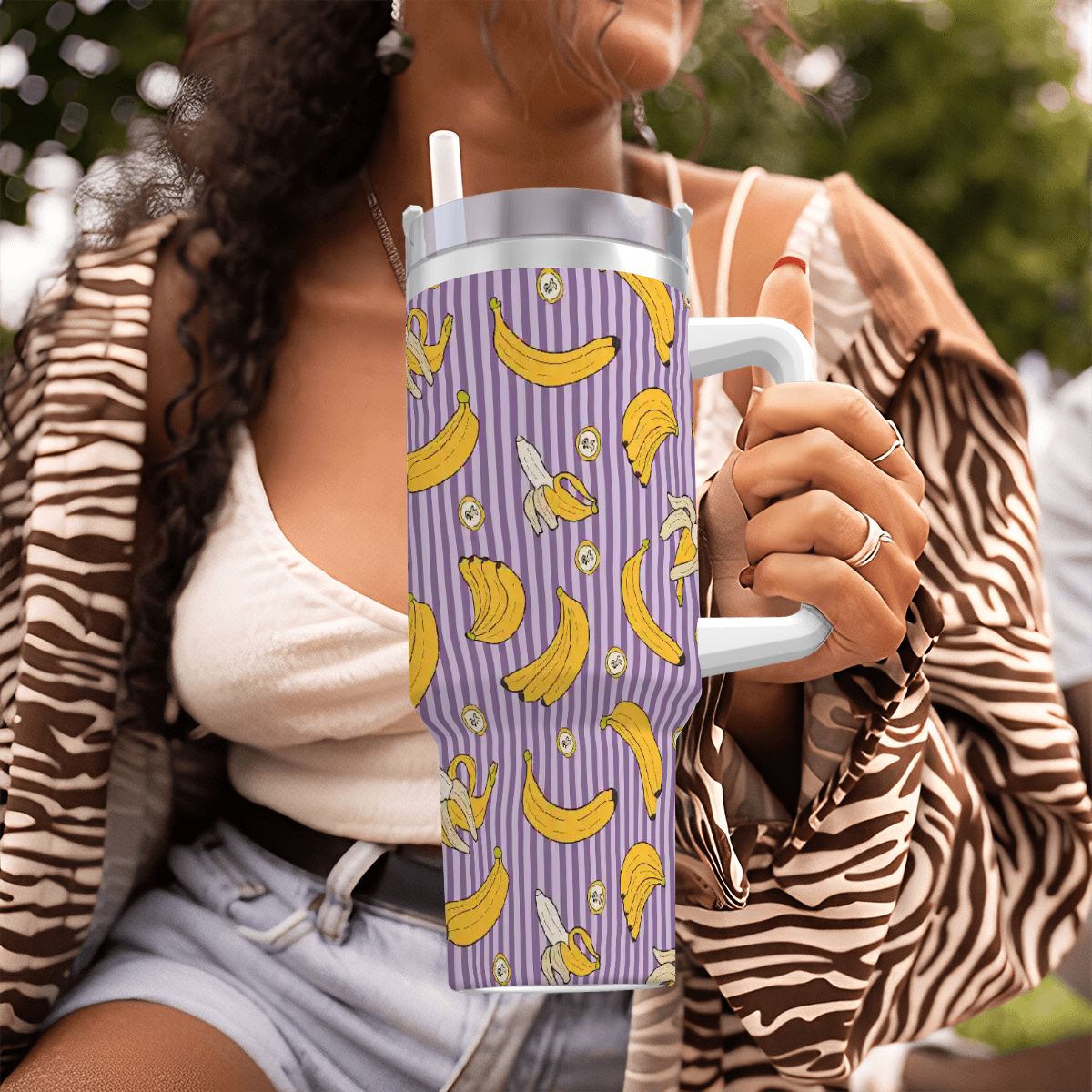 Person holding a purple tumbler with banana pattern outdoors