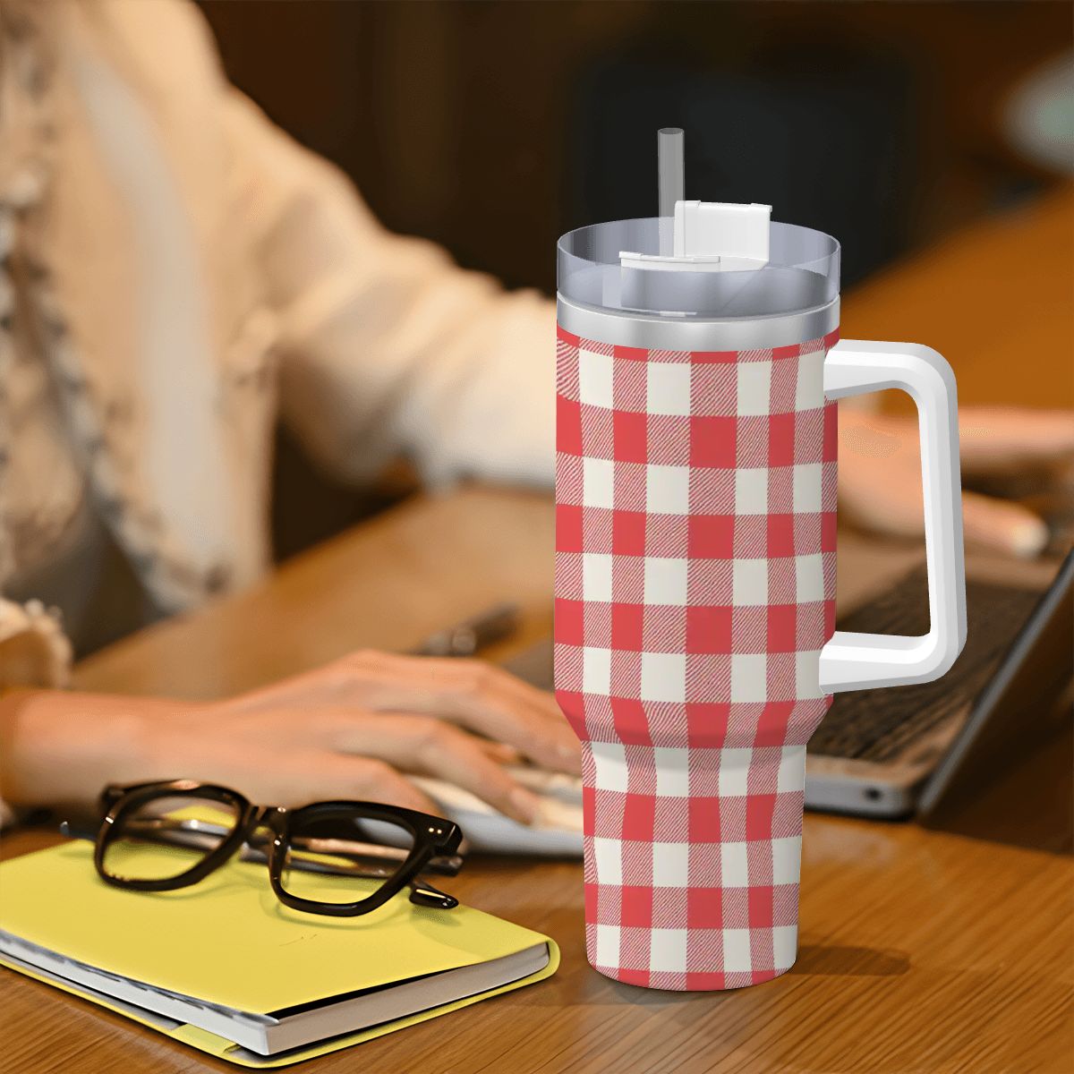 Red and white checkered mug with handle on a desk next to glasses and a notebook.