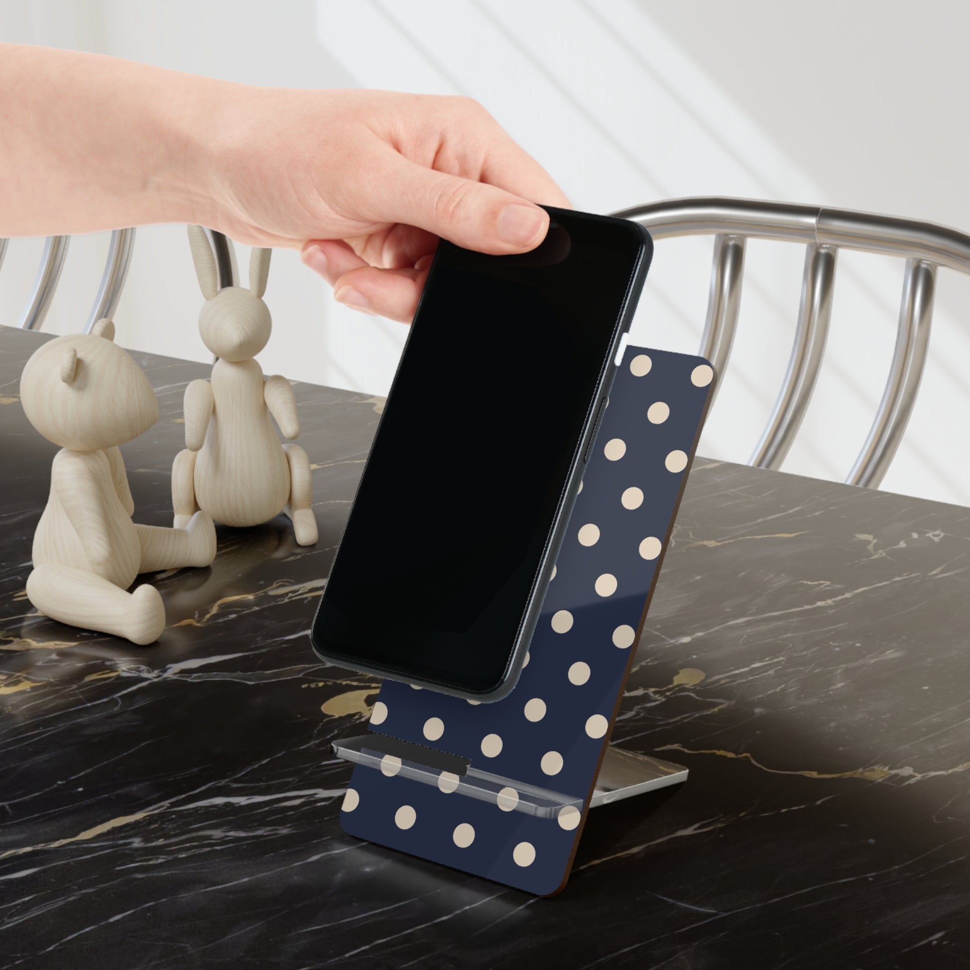 Person using a blue polka dot phone stand on a marble surface with decorative items.