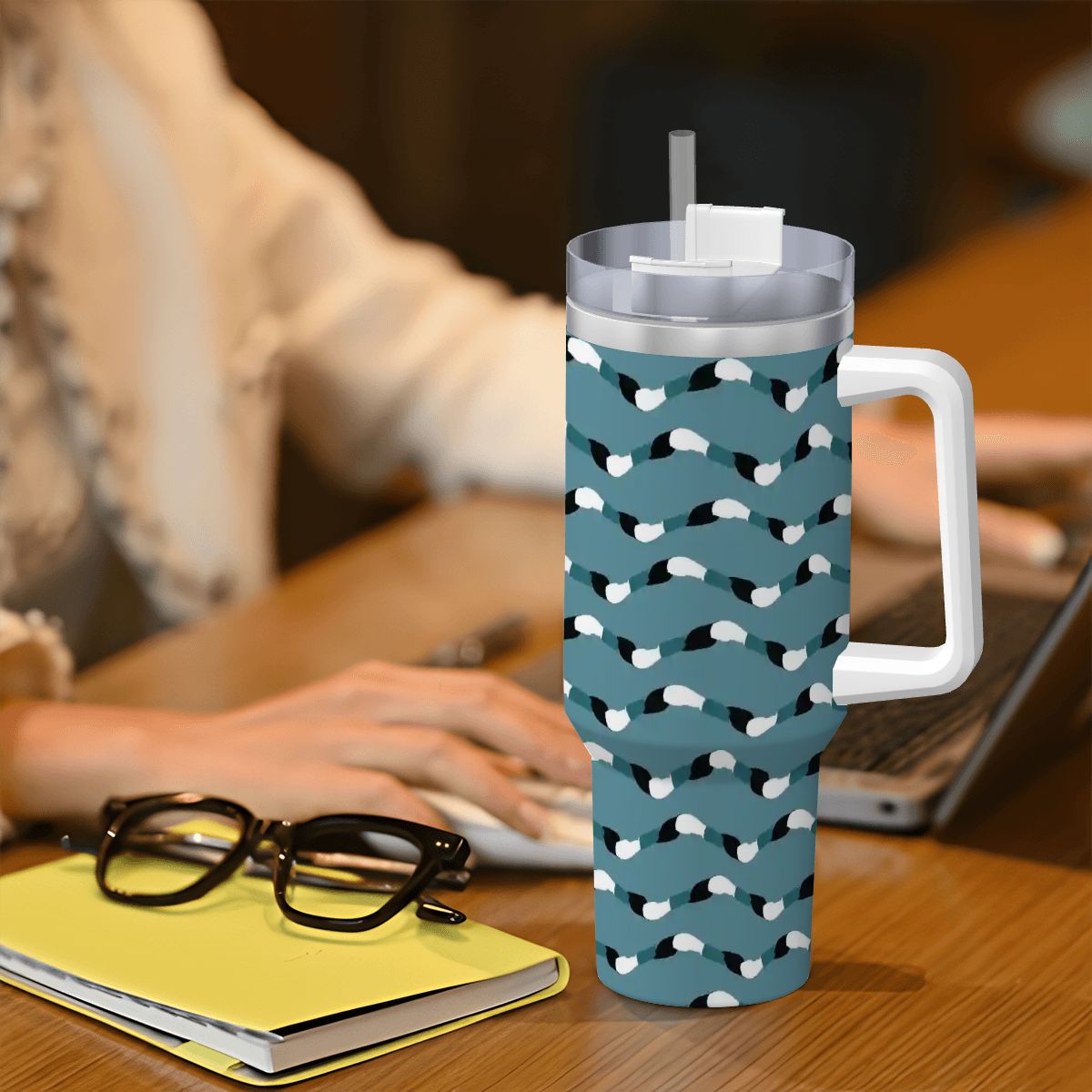 Blue mug with white pattern on a desk with a person using a laptop in the background