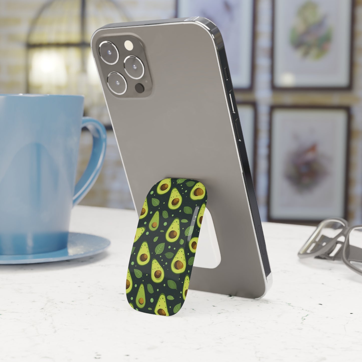 Phone with an avocado-patterned stand on a table next to a blue mug.