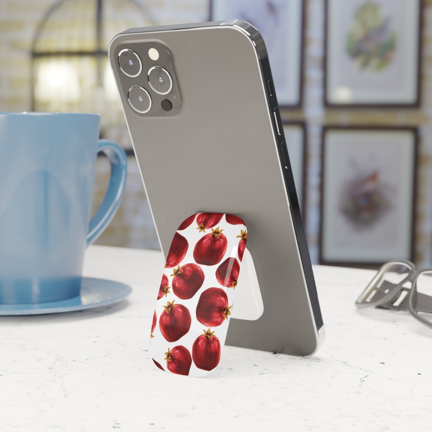 Phone case with red fruit design on a white surface next to a blue mug.