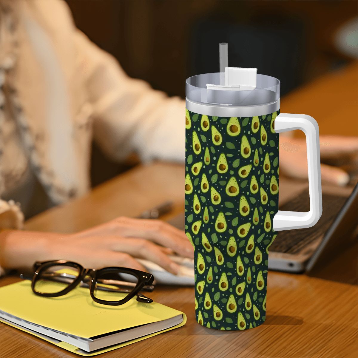 Tumbler with a feather pattern on a desk with a person using a laptop in the background