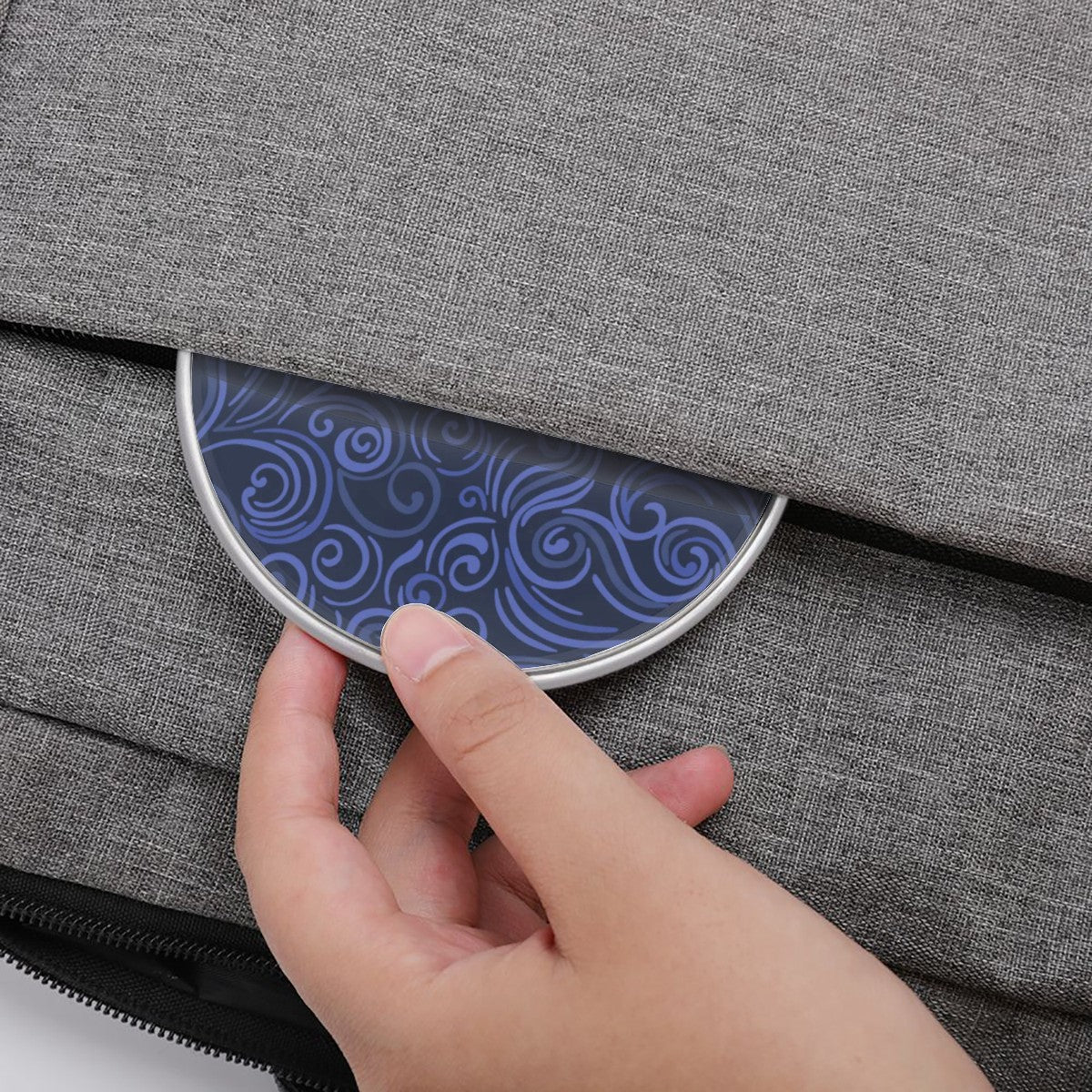 Hand opening a gray textured bag with a blue patterned flap.