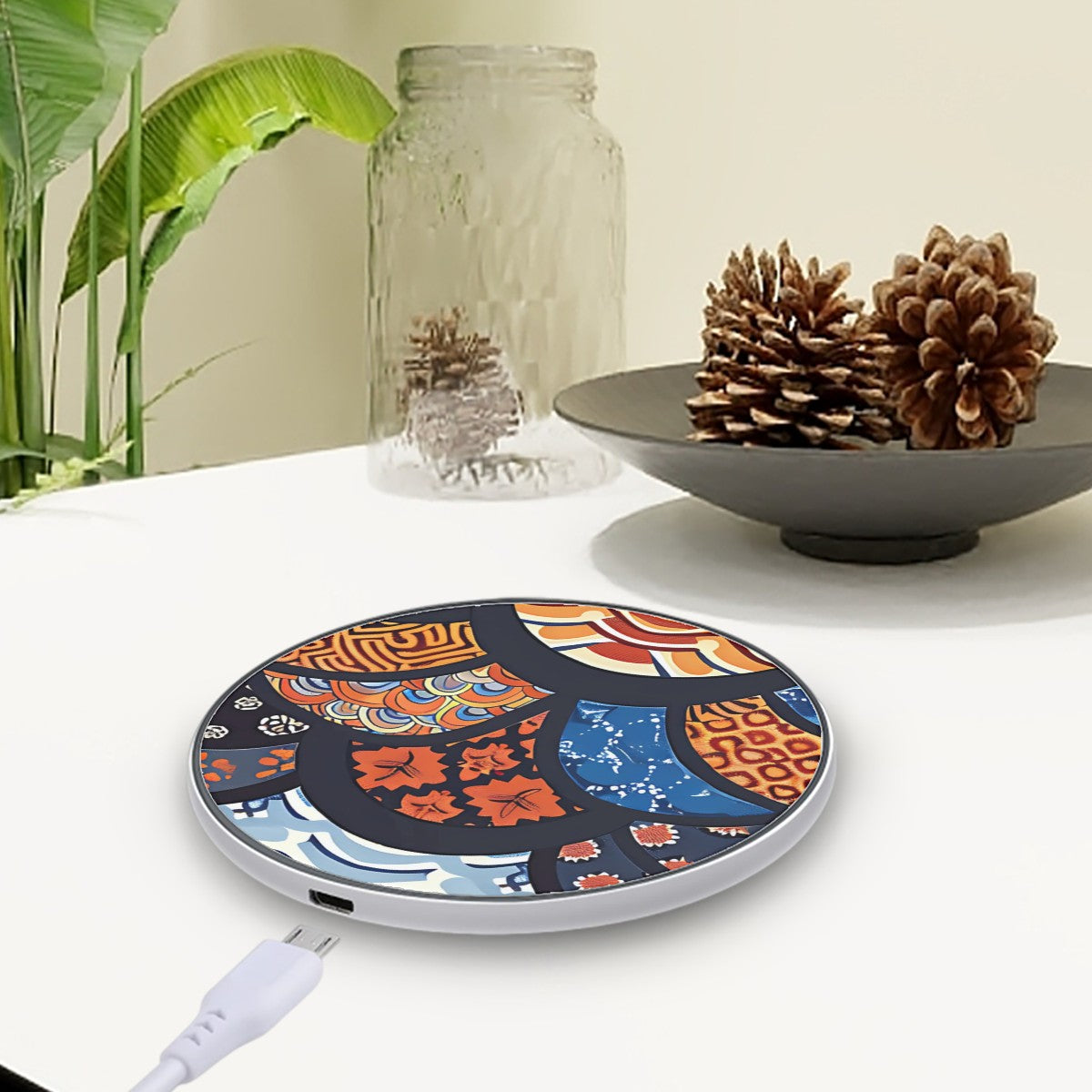 Decorative wireless charging pad with colorful design on a table with a plant and decorative bowl in the background. | Casenari