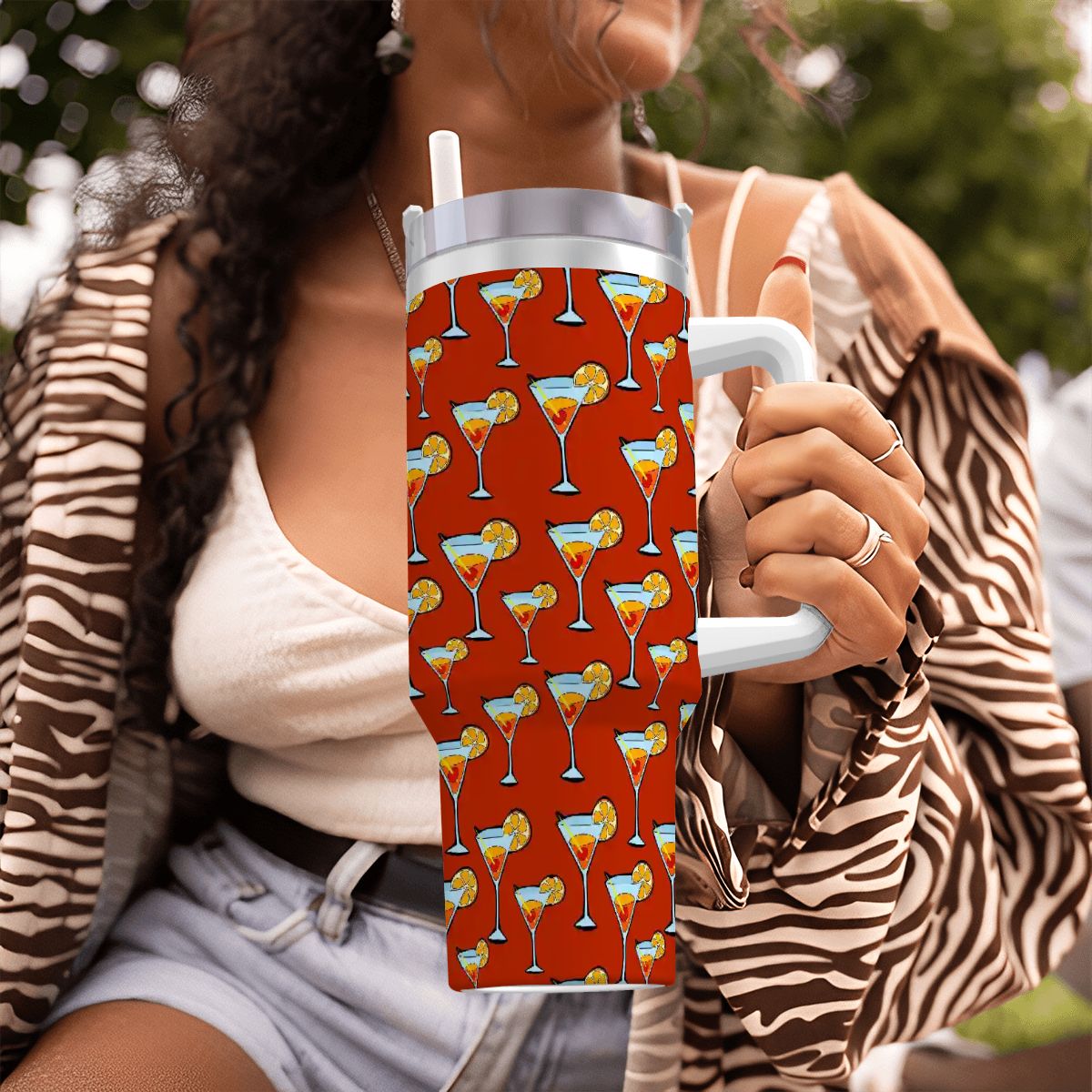 Person holding a red tumbler with cocktail pattern outdoors