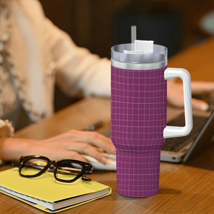 Purple grid-patterned tumbler with a white handle on a desk with a person using a laptop in the background.