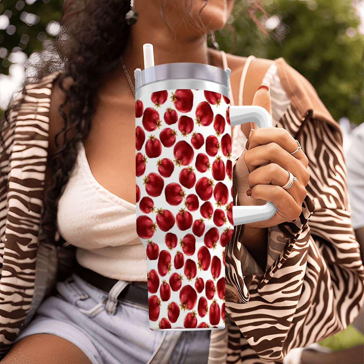 Person holding a tumbler with red apple pattern outdoors