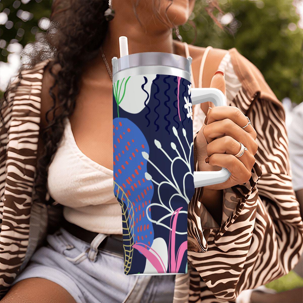 Person holding a colorful tumbler with a floral design outdoors