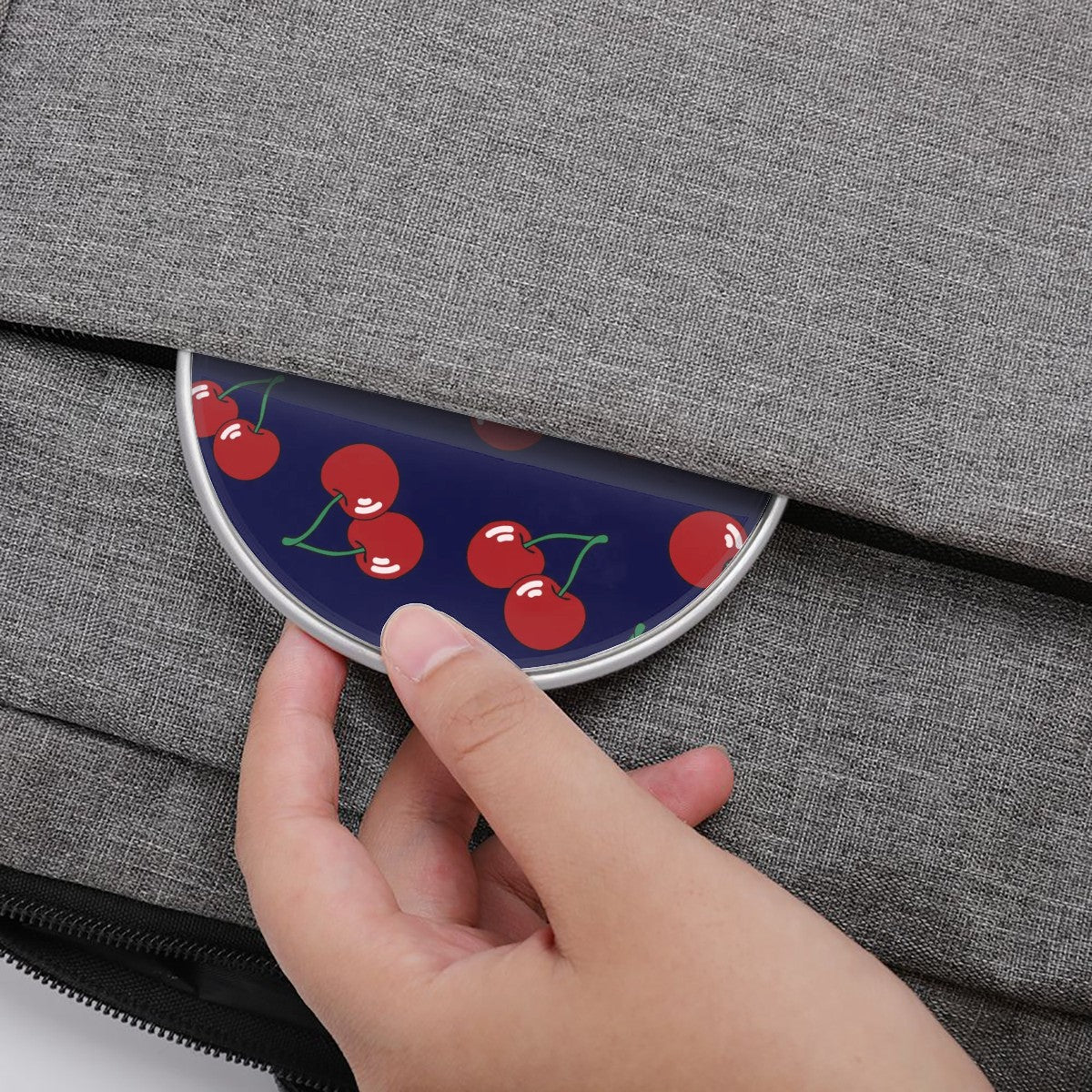 Hand holding a compact mirror with cherry design against a gray textured background