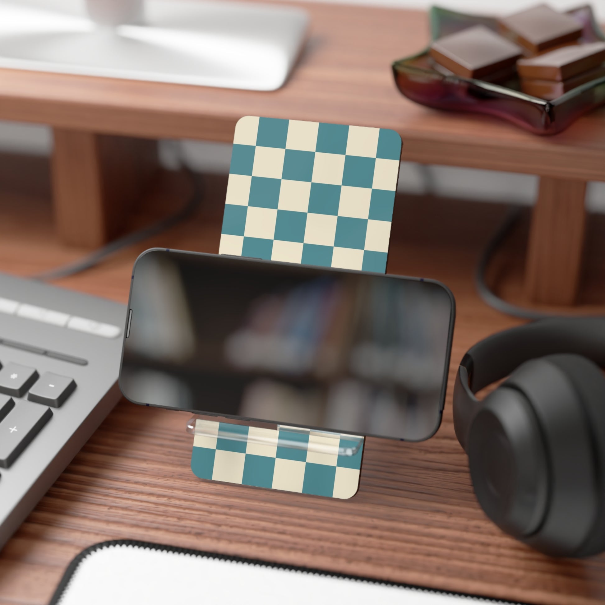 Desk setup with a smartphone stand, checkered card, keyboard, and headphones.