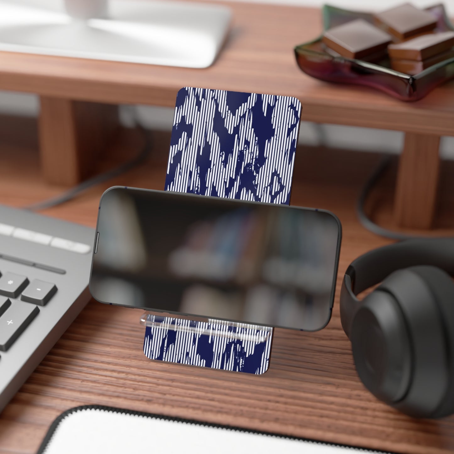 Phone stand with blue camouflage pattern on a desk with keyboard, mouse, and headphones.