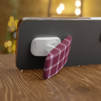 Phone with a pink and white checkered phone grip on a wooden surface with blurred lights in the background