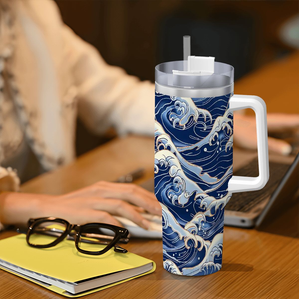 Tumbler with wave design on a desk with a person using a laptop.