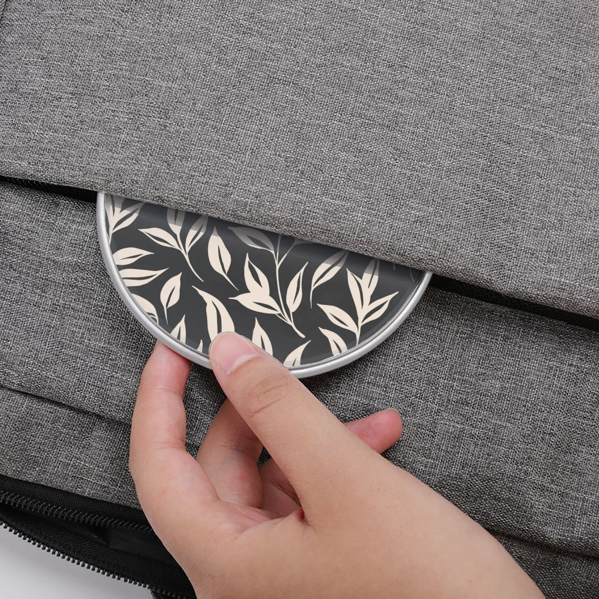 Hand placing a round pouch with leaf pattern into a gray textured bag.