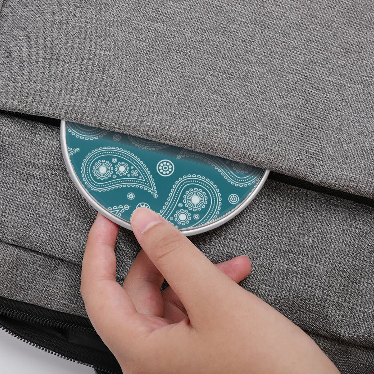 Hand placing a teal and white patterned coaster onto a gray fabric surface