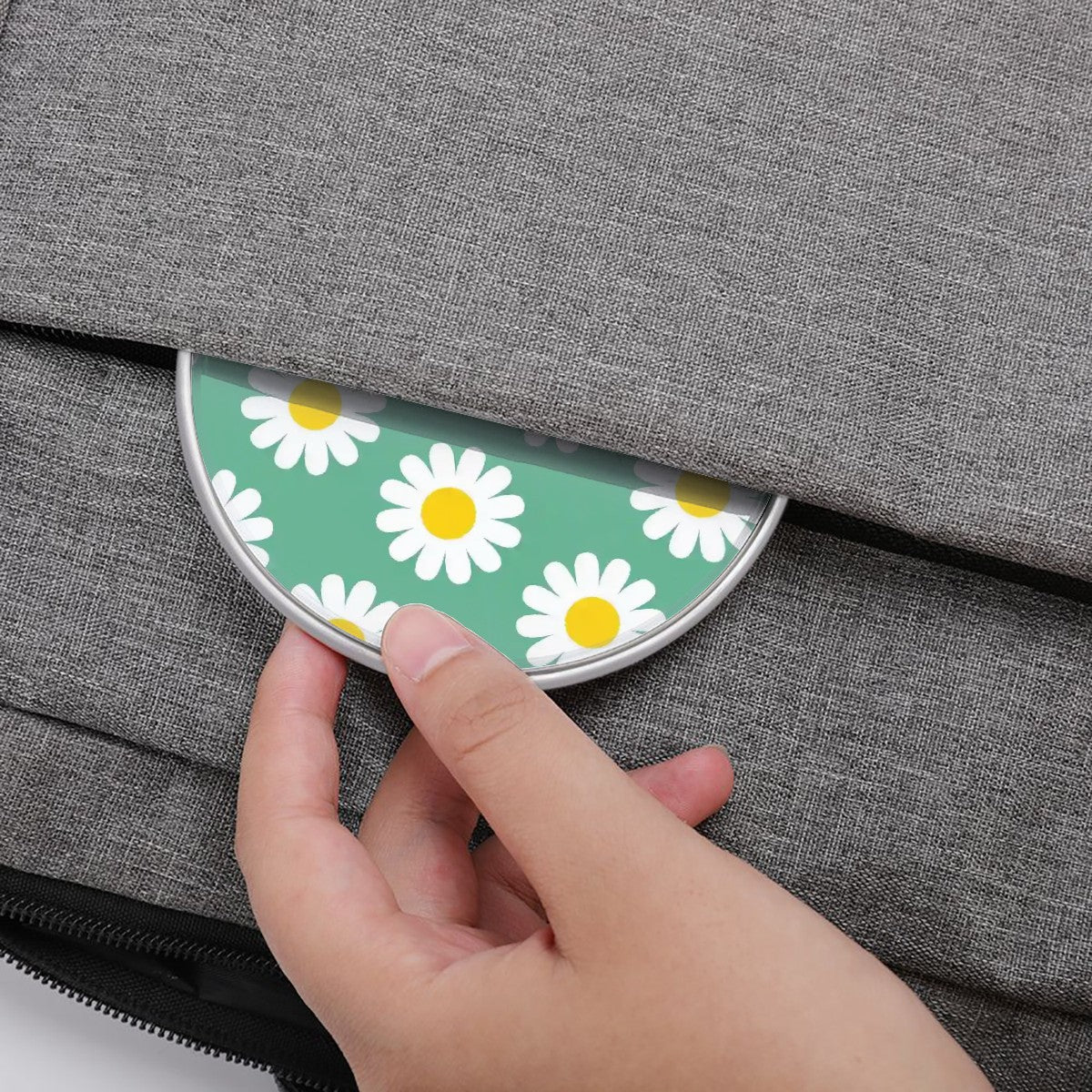 Hand placing a compact mirror with daisy pattern on a gray textured surface