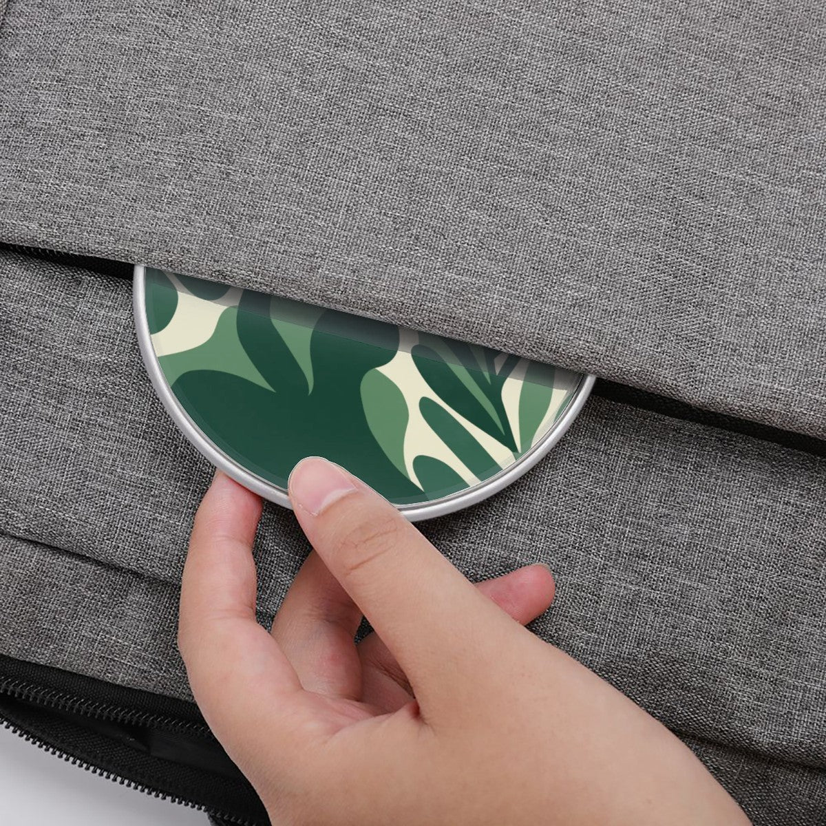 Hand placing a round, green leaf-patterned coaster onto a gray textured surface.