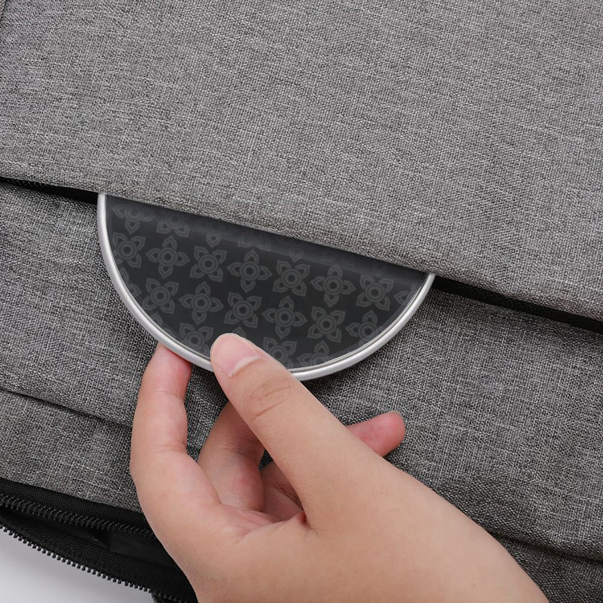 Hand opening a gray textured bag with a circular metallic handle.