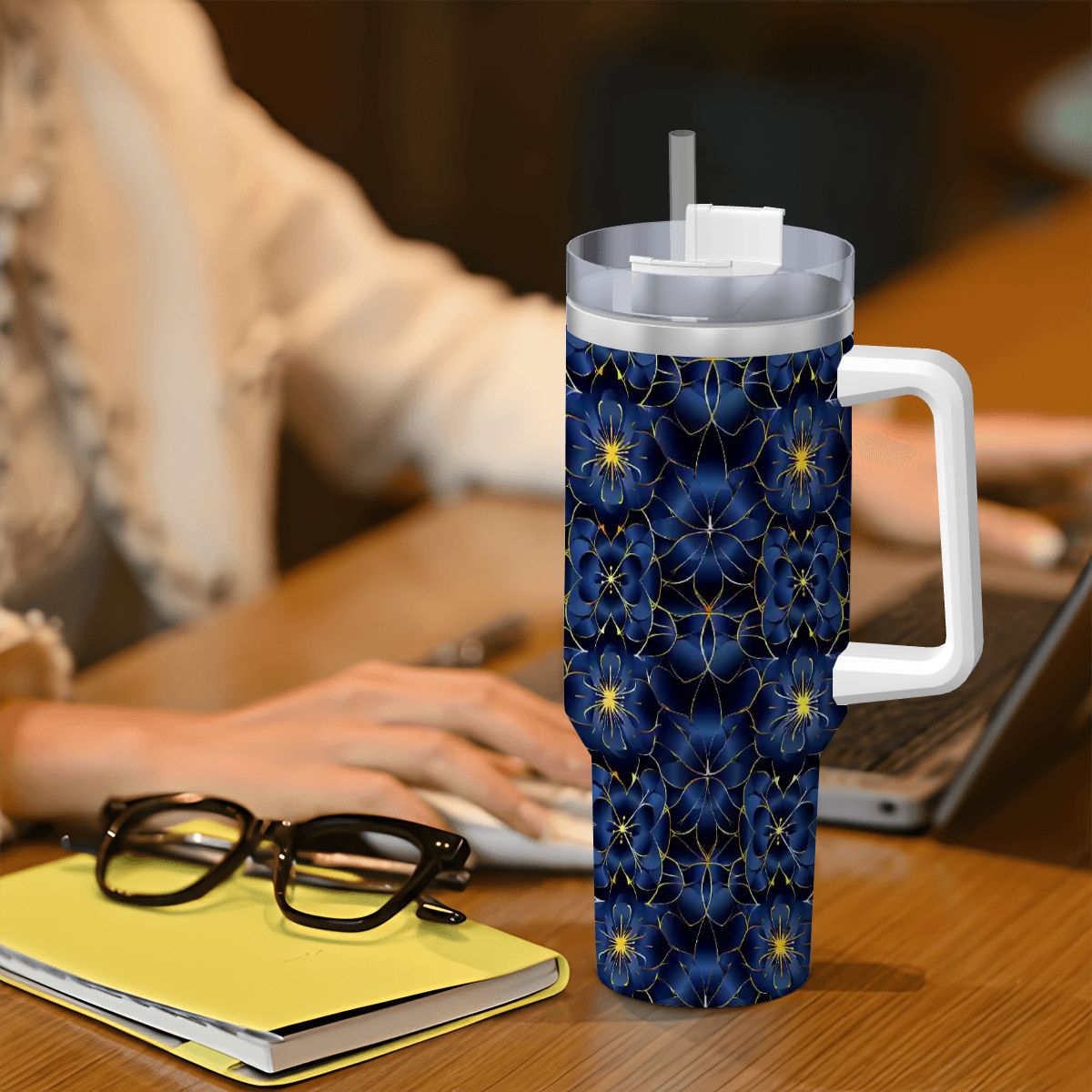 Floral-patterned tumbler on a desk with a person using a laptop in the background