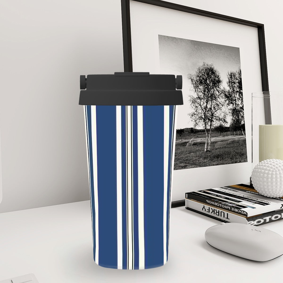 Blue and white striped trash can on a desk with a framed picture and books in the background.