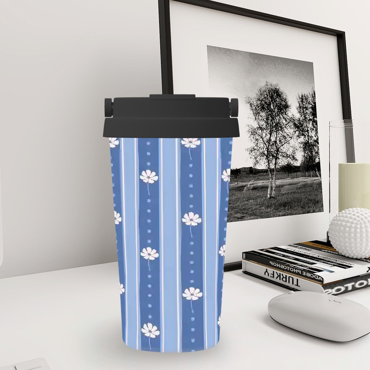 Blue striped tumbler with white flowers on a desk next to a framed picture and books.