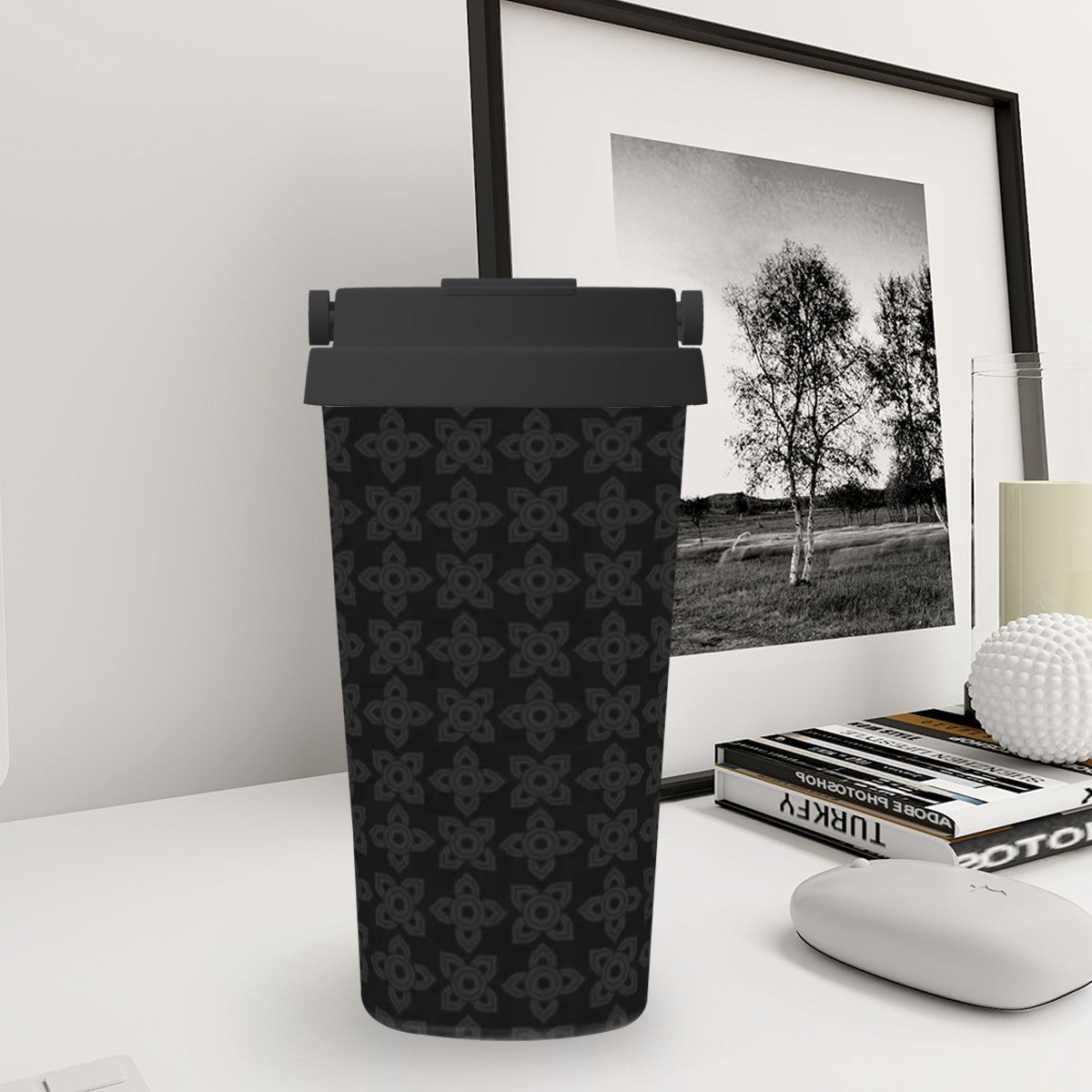 Black patterned tumbler on a white surface with a framed black and white photo in the background.