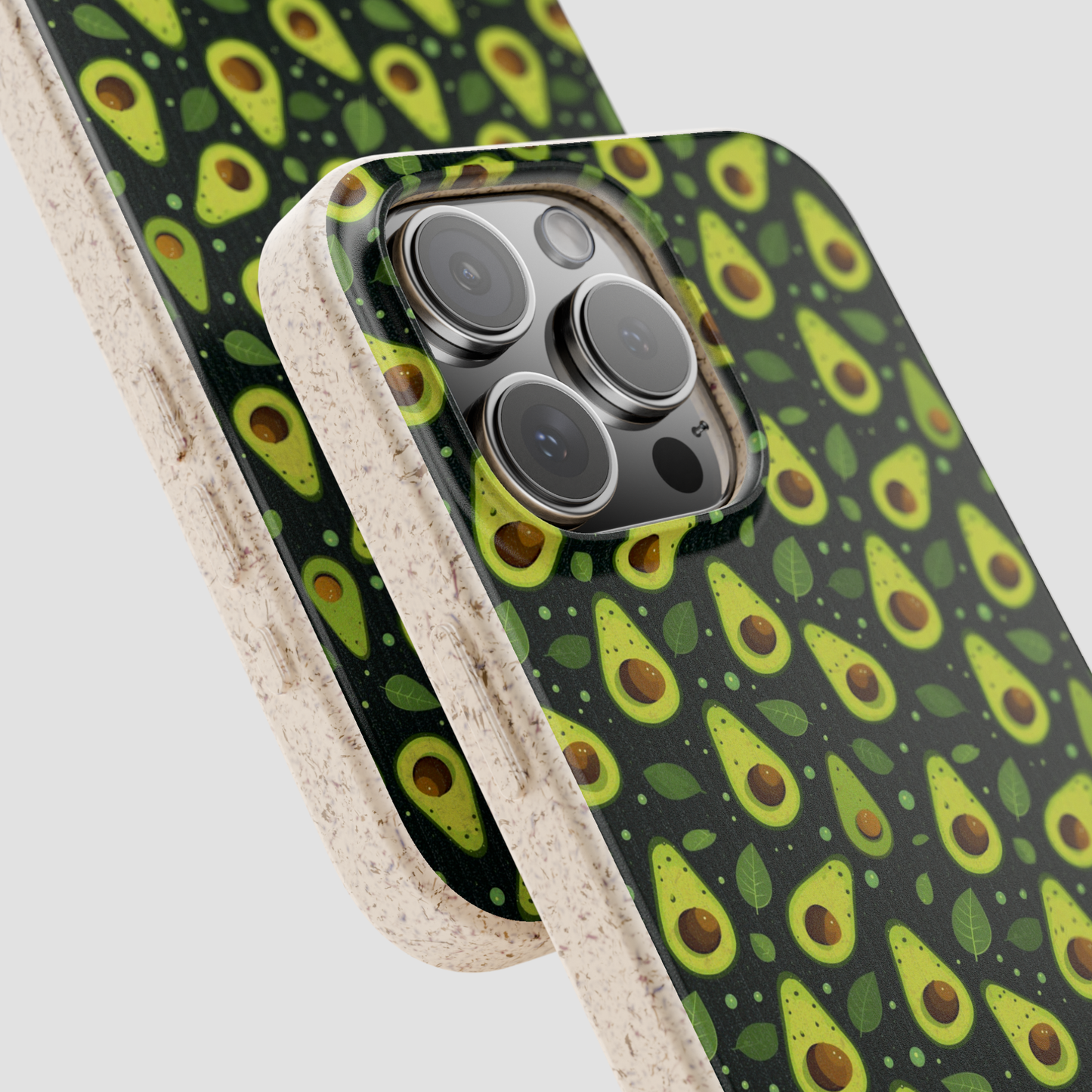 A close-up of a smartphone case with a repeating avocado print on a dark background, shown layered over another phone case. The case has a glossy printed back and a textured beige side bumper, photographed on a light gray background.