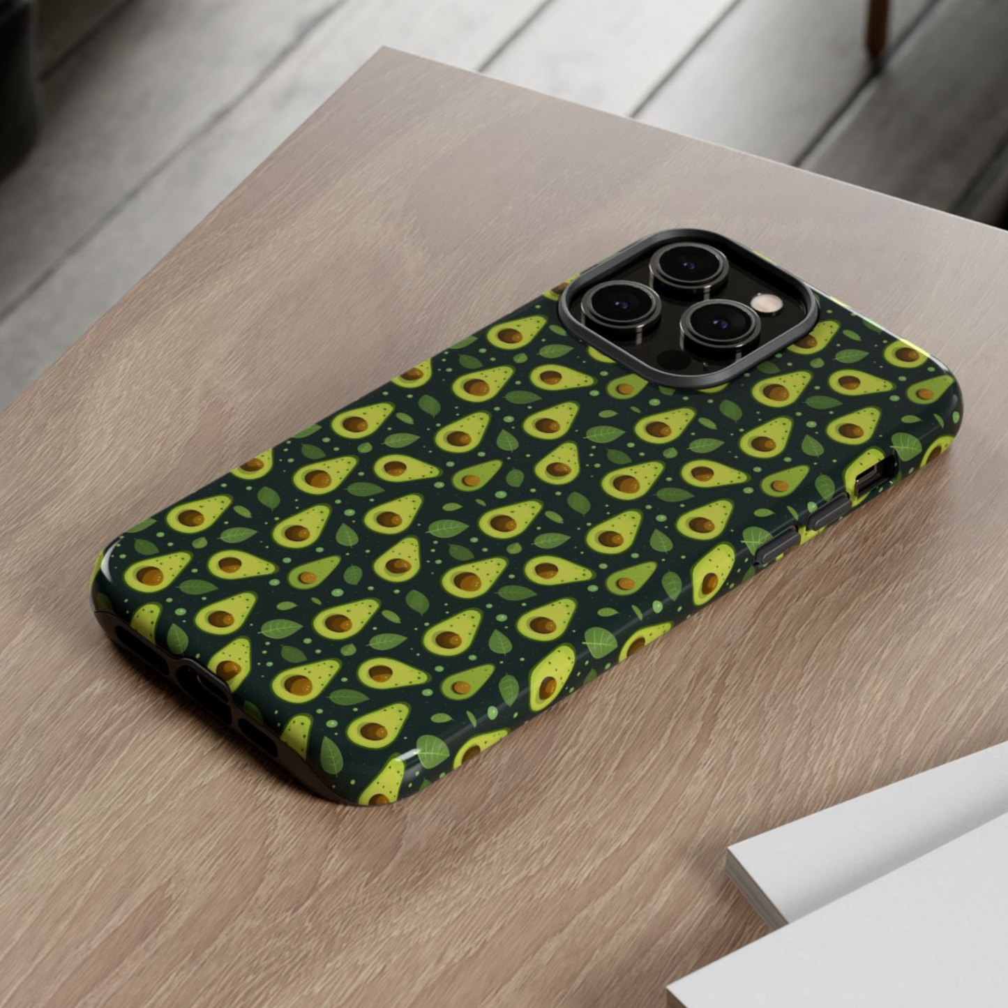 A phone case with a repeating avocado print pattern, shown resting on a light brown wooden tabletop.