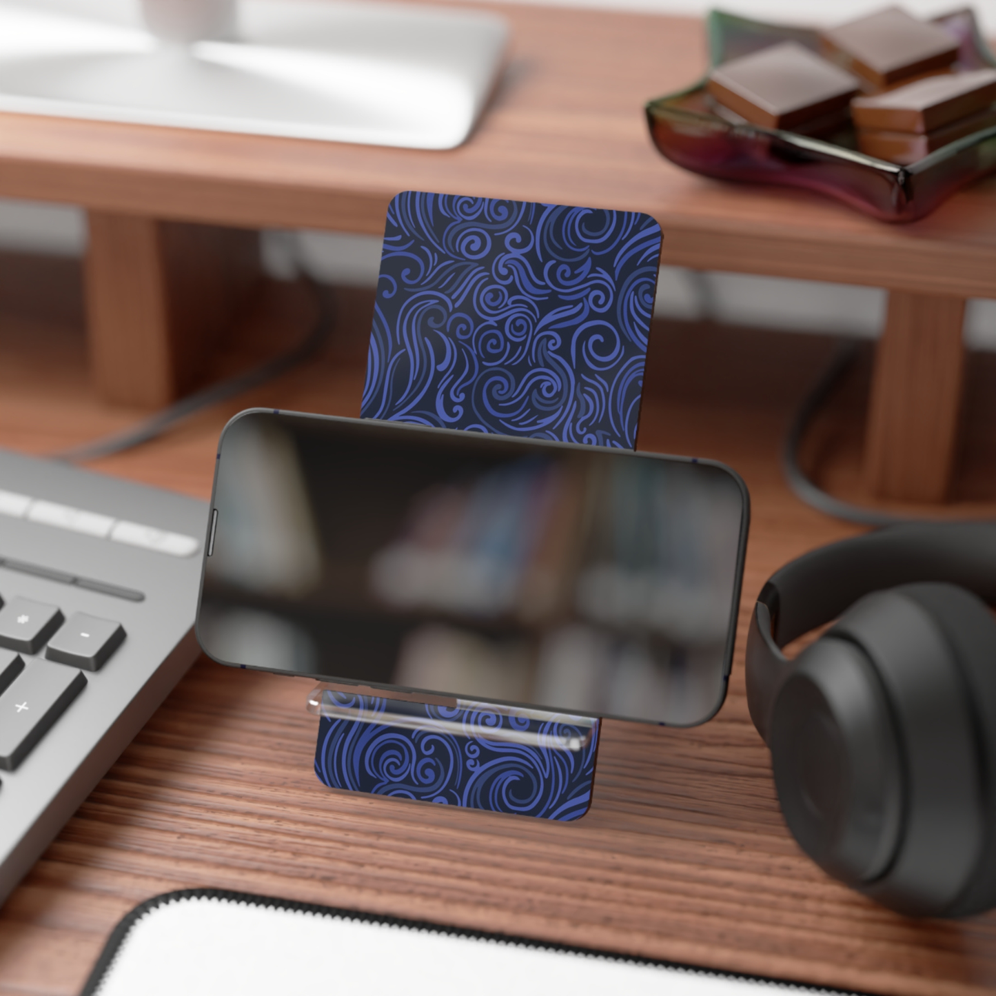 Phone stand with blue floral design on a desk with keyboard, mouse, and headphones.