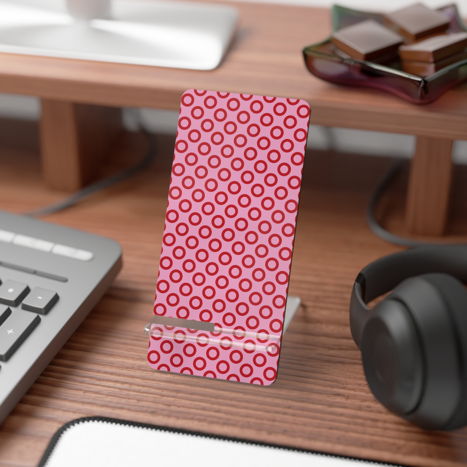 Pink phone case with red circular pattern on a desk with keyboard and headphones