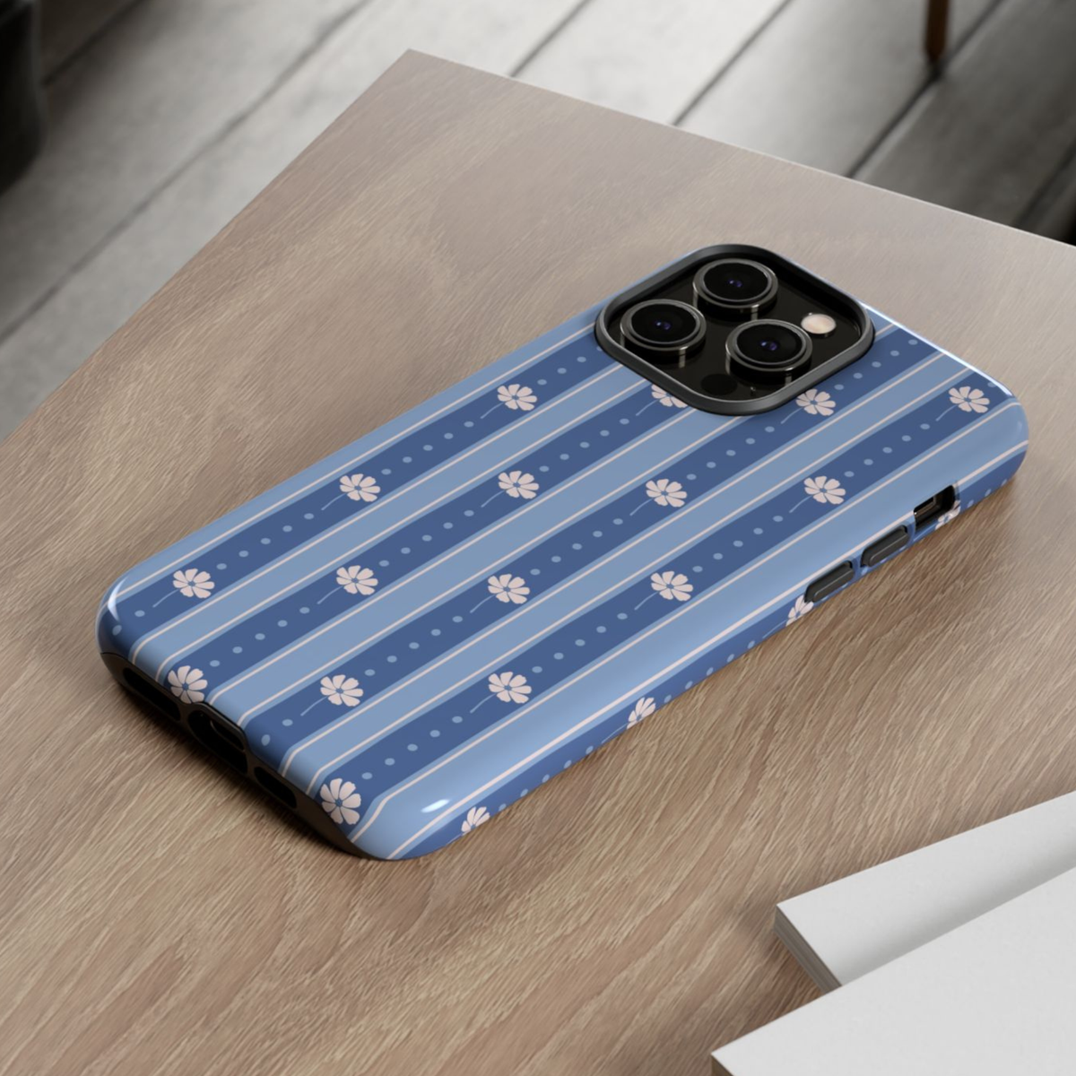 A blue striped phone case with white floral motifs, shown on a wooden tabletop.