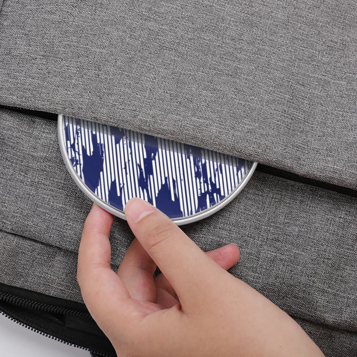 Hand placing a blue and white patterned object into a gray fabric bag.