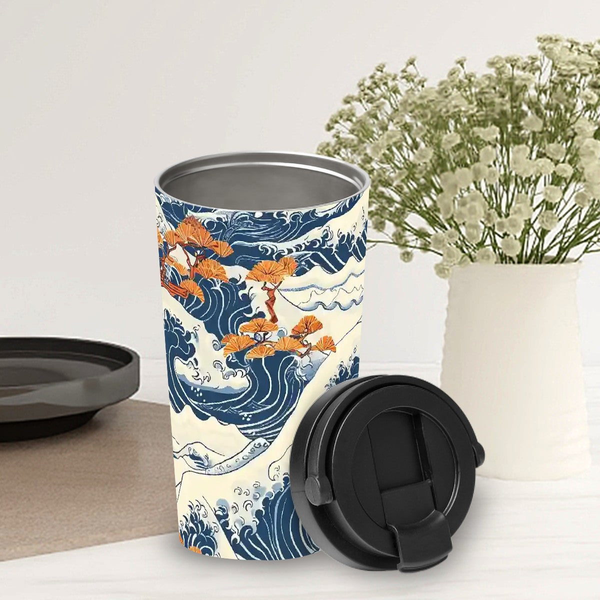 Tumbler with wave and orange fish design on a white surface with a vase of flowers in the background. | Casenari