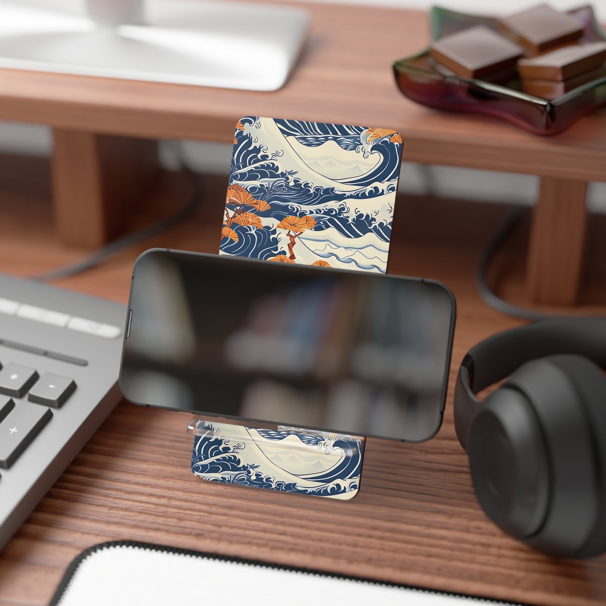Phone stand with wave design on a desk with keyboard, headphones, and books.
