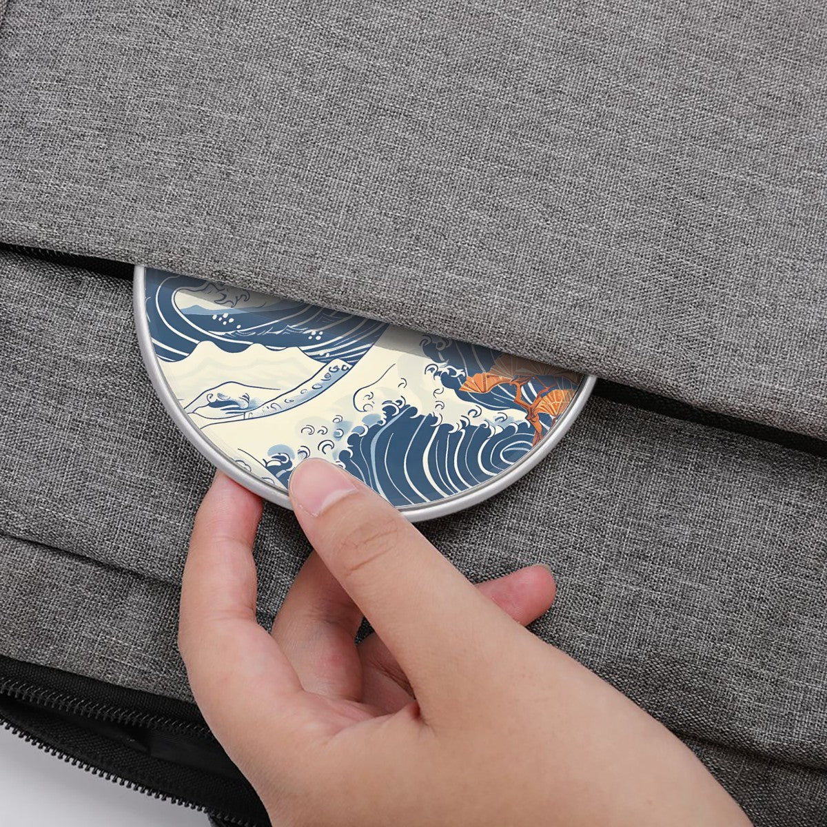 Hand placing a circular object with wave design into a gray fabric bag | Casenari