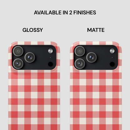 Two smartphone cases shown side by side on a light gray background, labeled GLOSSY and MATTE under the text 'AVAILABLE IN 2 FINISHES.' Both cases have a red and off-white gingham check pattern with black camera cutouts.
