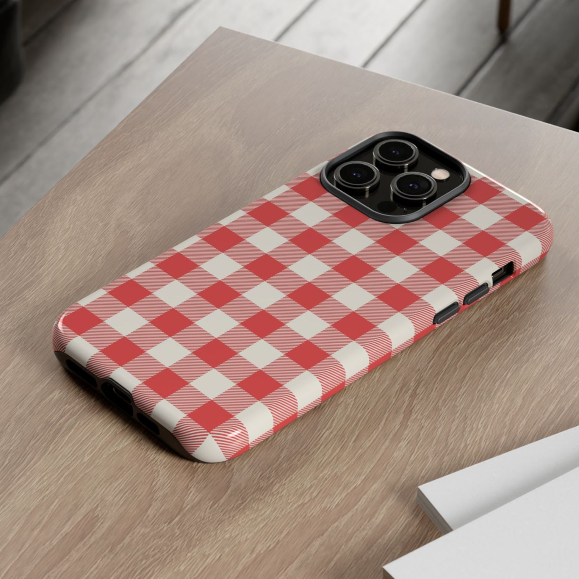 A phone case with a red and white gingham checkered pattern, shown on a smartphone resting on a light wood tabletop.