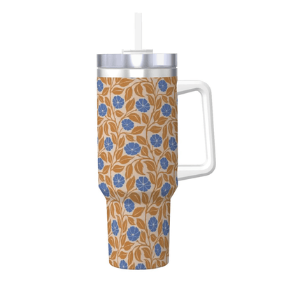 A handled tumbler with a clear plastic handle, a white straw, and a wrap-around floral pattern in blue and brown on a cream background, shown on a plain white background.