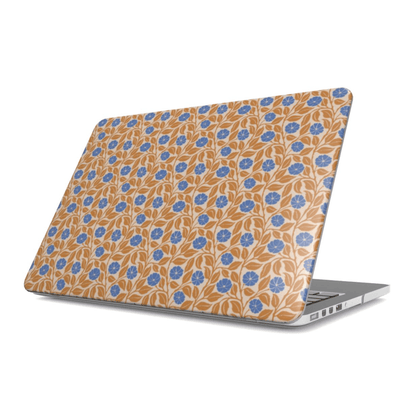 A silver laptop with a protective skin featuring a repeating blue floral and leaf pattern on a warm tan background, shown from a three-quarters angle against a white background.