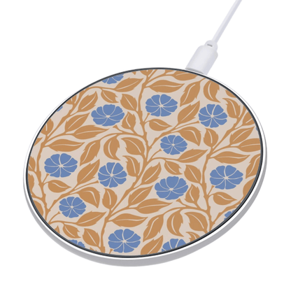 A round wireless charging pad with a beige background, a blue and tan floral pattern, and a white charging cable plugged in, shown on a white background.