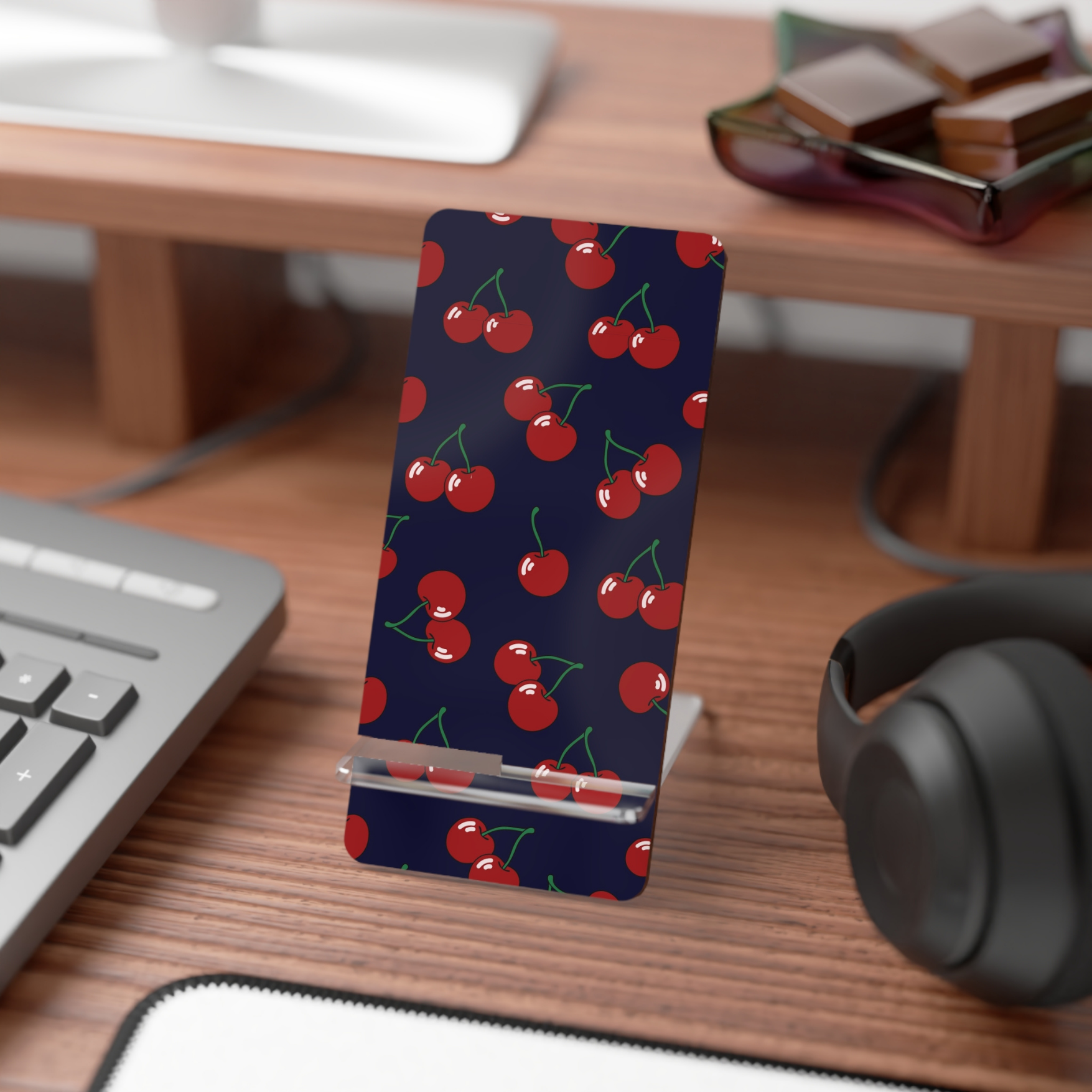 Phone stand with cherry pattern on a desk with keyboard, mouse, and headphones.