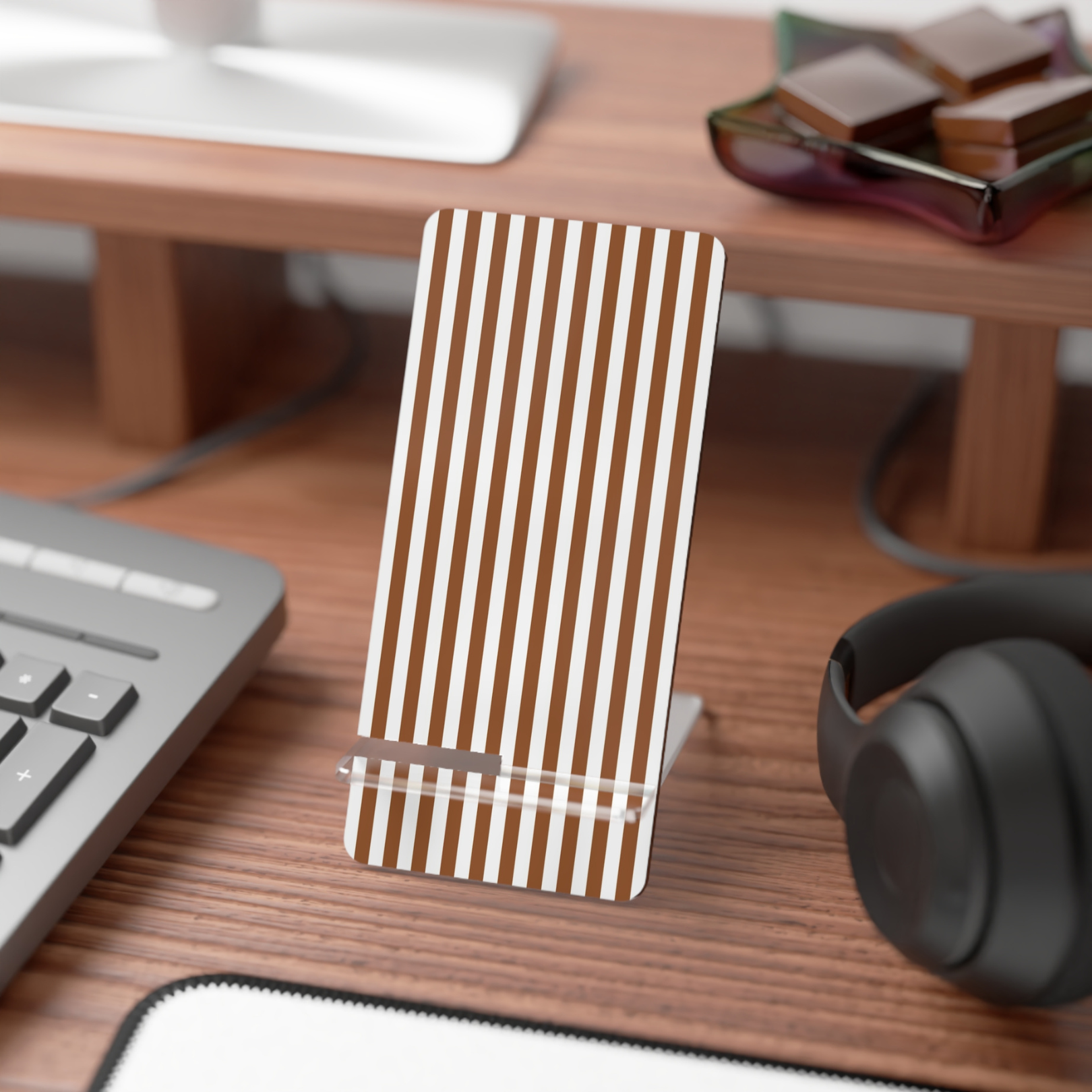 Wooden phone stand with striped design on a desk with keyboard, mouse, and headphones.
