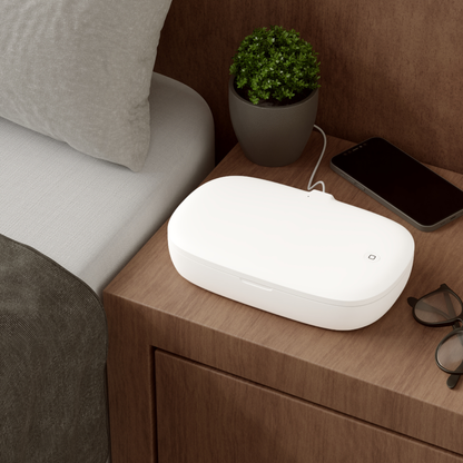 White electronic device on a wooden nightstand with a phone and plant in the background