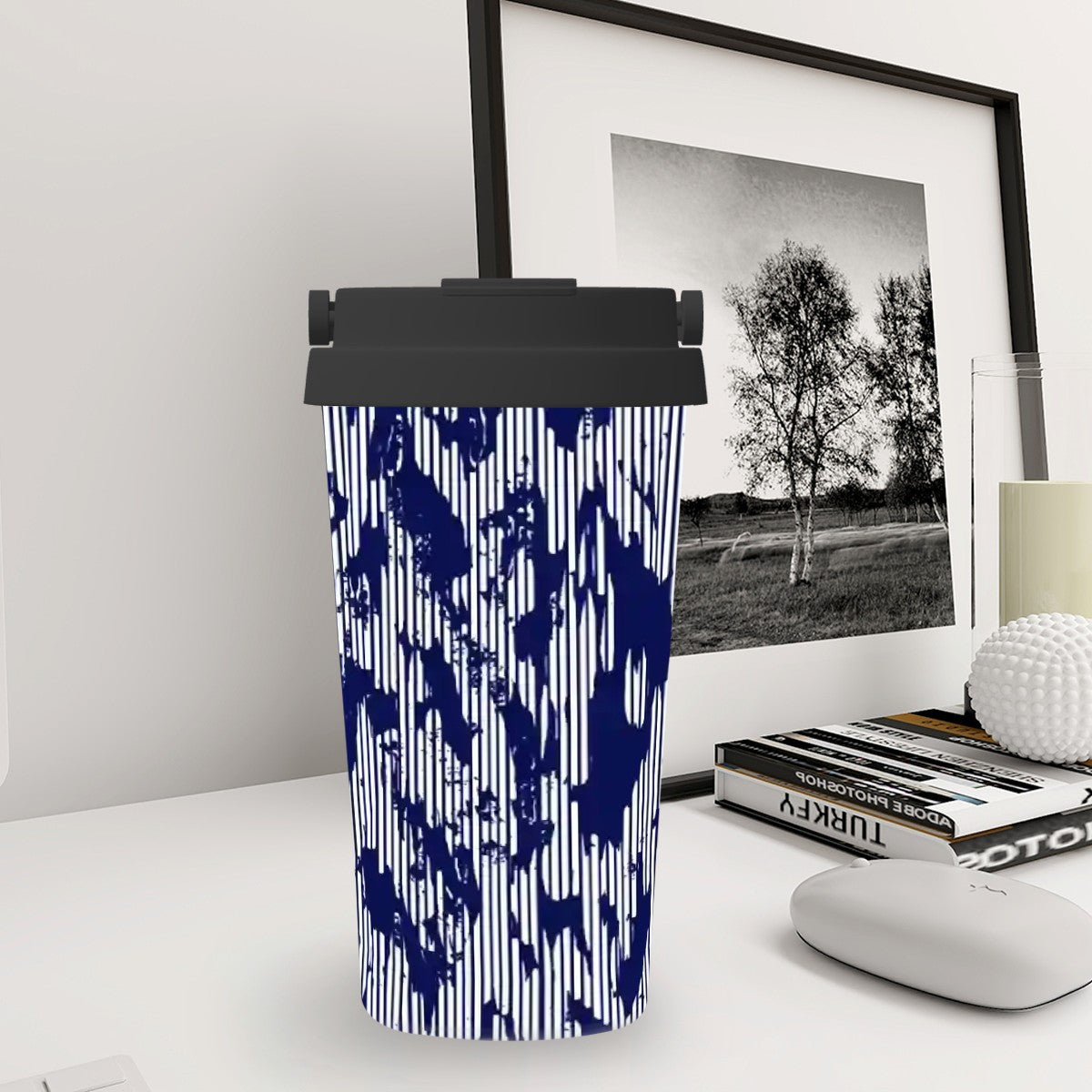 Tumbler with blue abstract pattern on a desk with books and a framed picture in the background