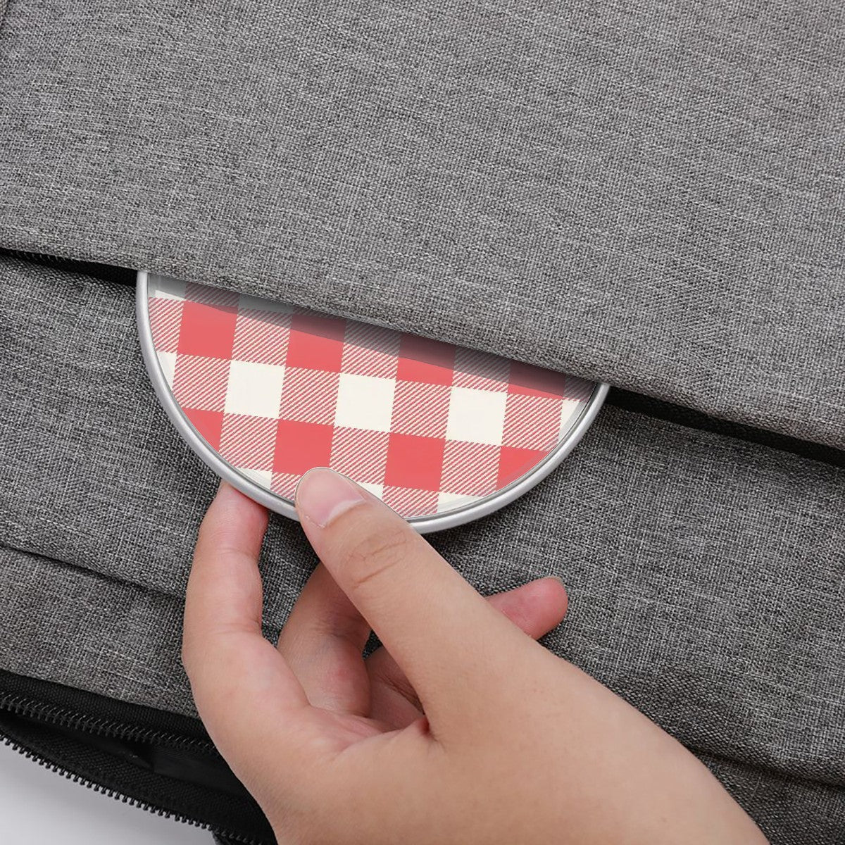 Hand opening a gray bag with a red and white checkered flap