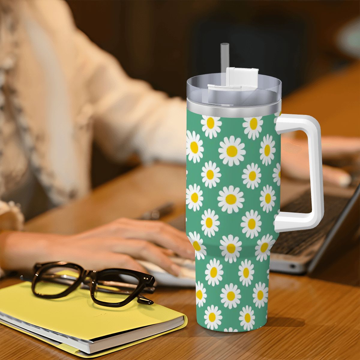 Tumbler with daisy pattern on a desk with a person using a laptop.