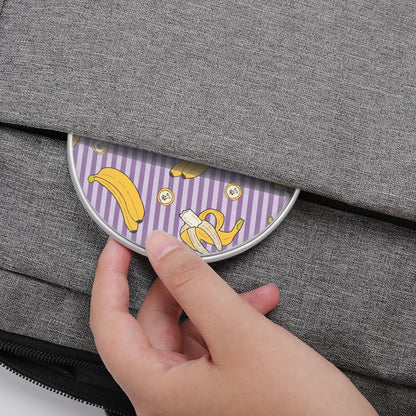 Hand placing a round purple coaster with banana design into a gray fabric bag.
