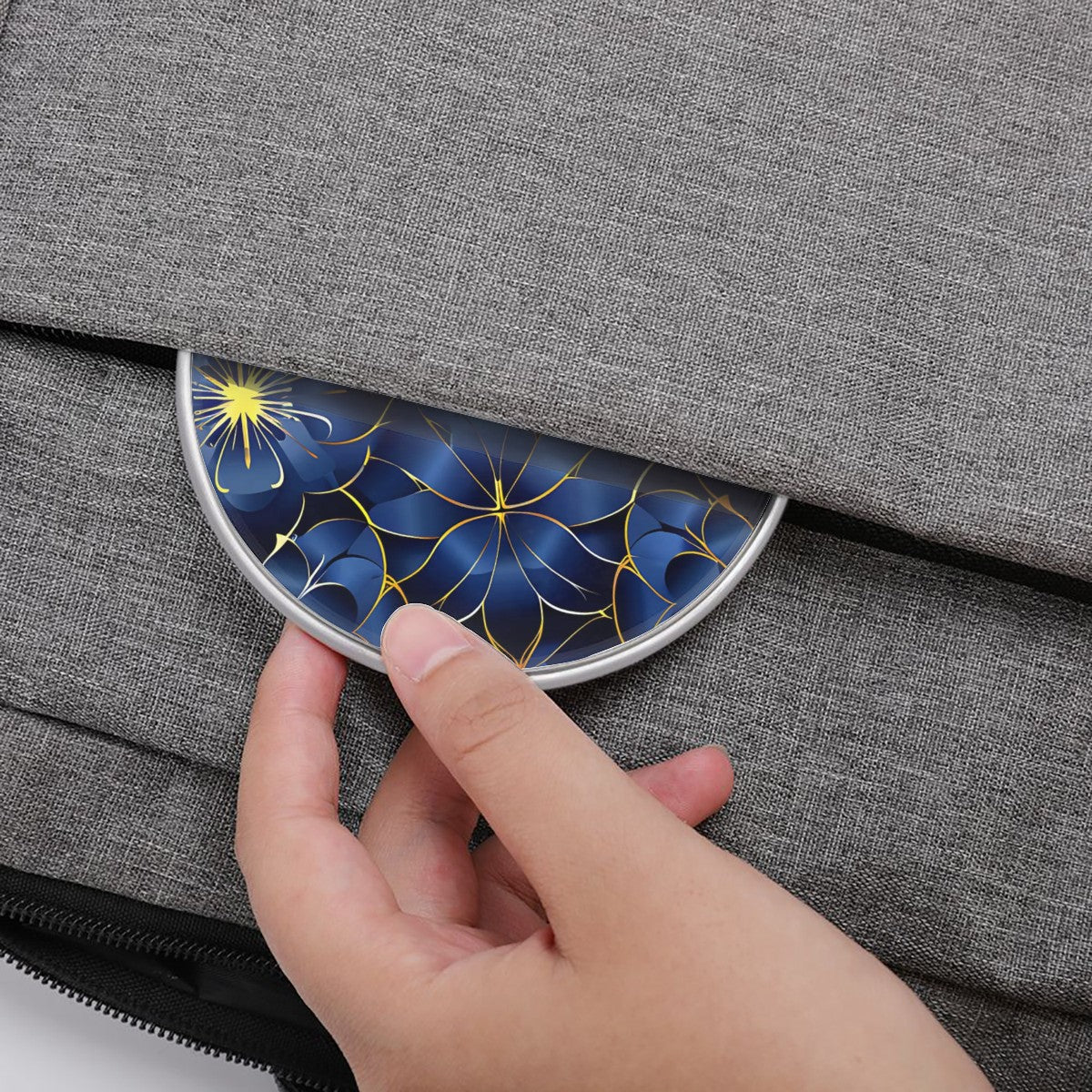 Hand placing a decorative blue and gold item into a gray fabric bag
