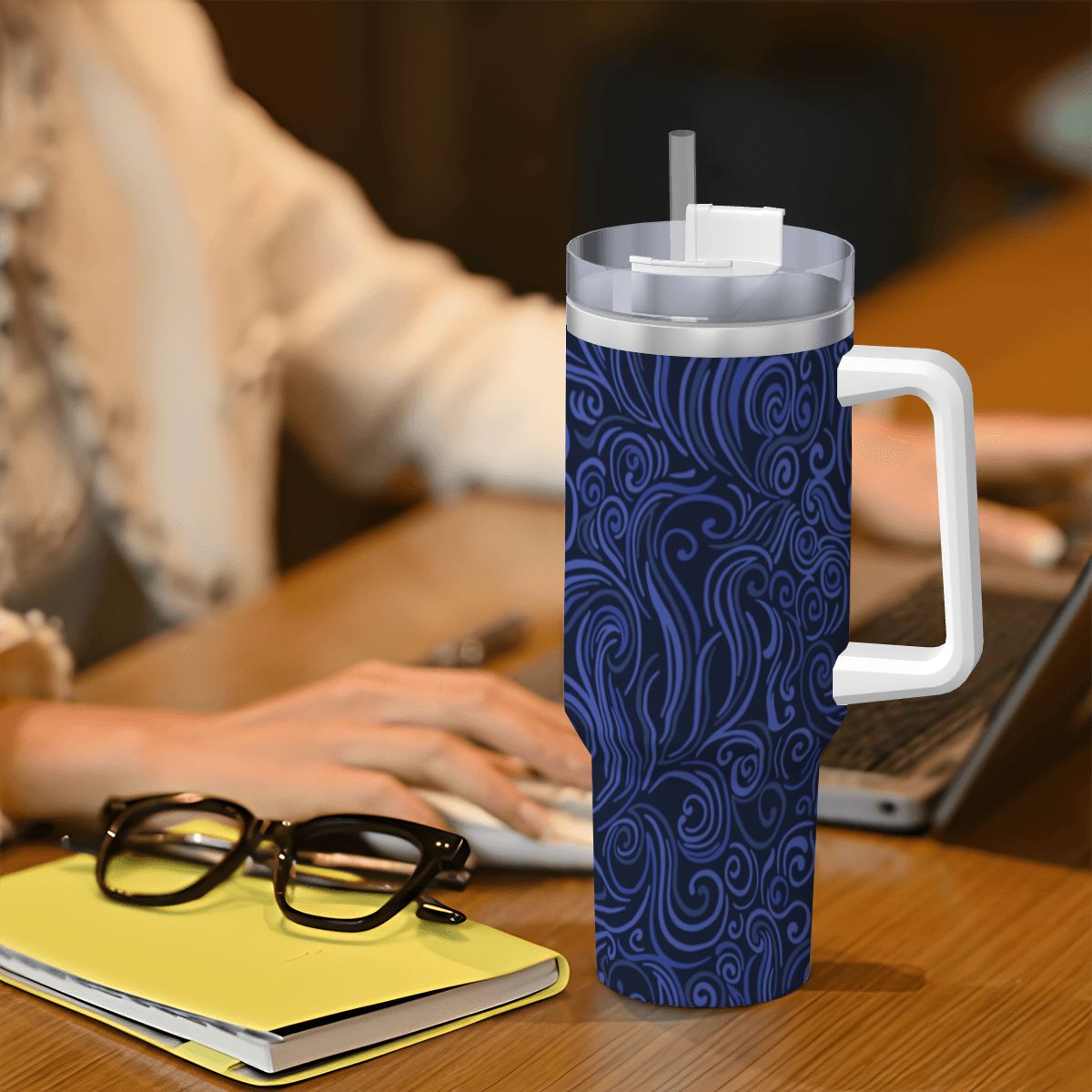 Blue patterned tumbler with a white handle on a desk next to a person using a laptop.